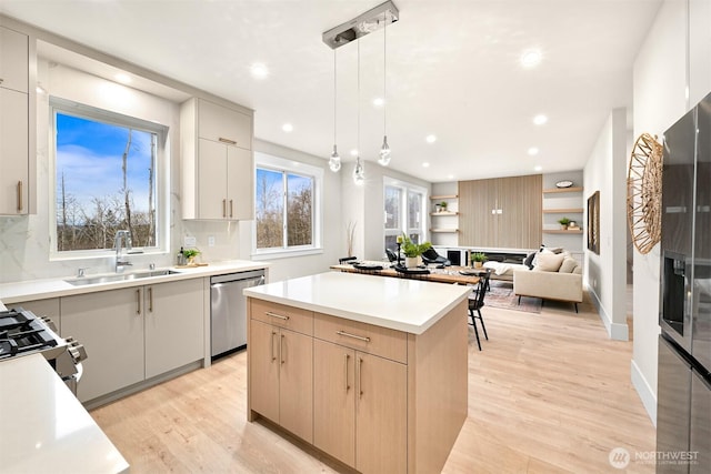 kitchen featuring stainless steel appliances, light countertops, hanging light fixtures, a sink, and a kitchen island