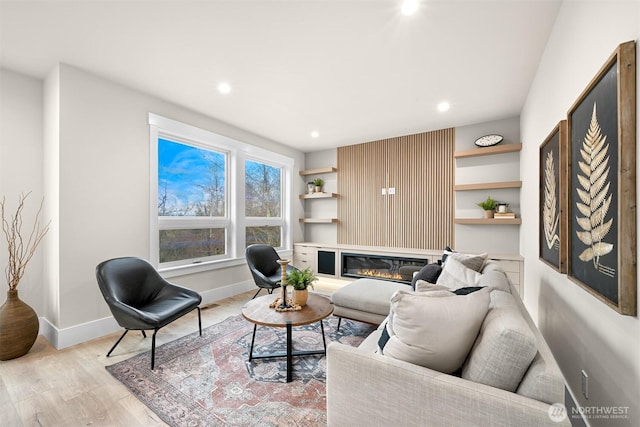 living room with a glass covered fireplace, baseboards, light wood finished floors, and recessed lighting