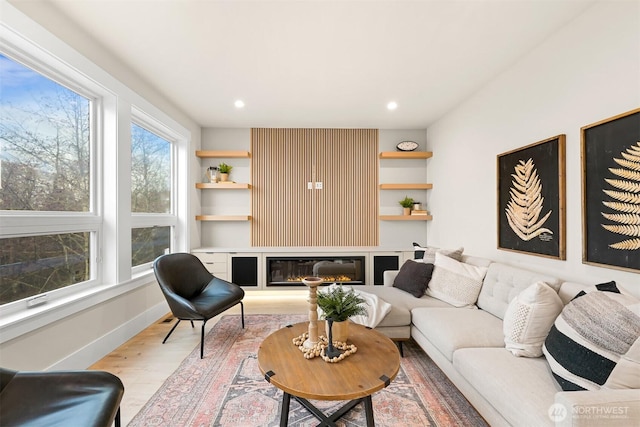 living area featuring built in shelves, recessed lighting, baseboards, light wood-style floors, and a glass covered fireplace