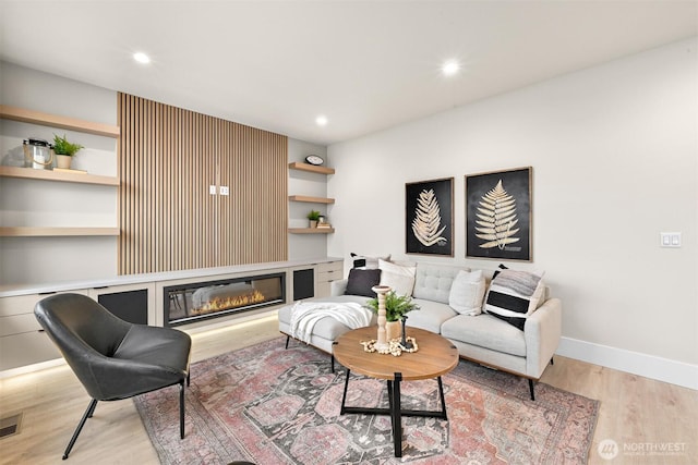 living area with baseboards, recessed lighting, a glass covered fireplace, and light wood-style floors