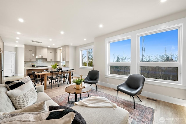 living room featuring light wood-type flooring, visible vents, baseboards, and recessed lighting