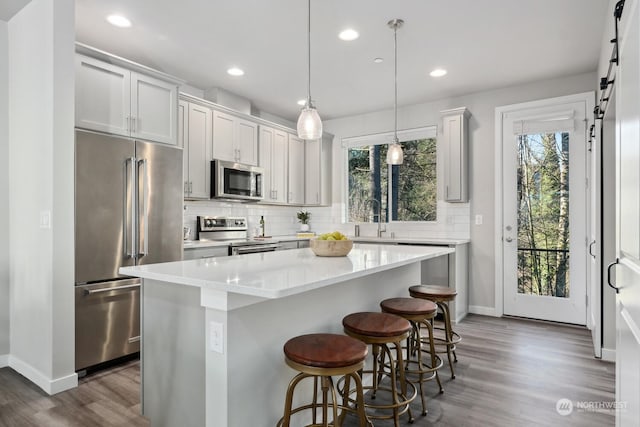 kitchen with stainless steel appliances, a center island, decorative backsplash, decorative light fixtures, and a barn door