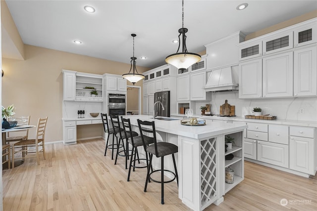 kitchen with white cabinetry, a kitchen island with sink, a kitchen bar, decorative light fixtures, and custom exhaust hood