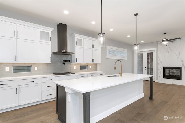 kitchen with stainless steel gas cooktop, sink, white cabinetry, a center island with sink, and wall chimney range hood