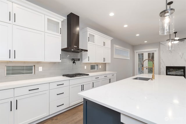 kitchen with sink, white cabinetry, hanging light fixtures, stainless steel gas stovetop, and wall chimney range hood