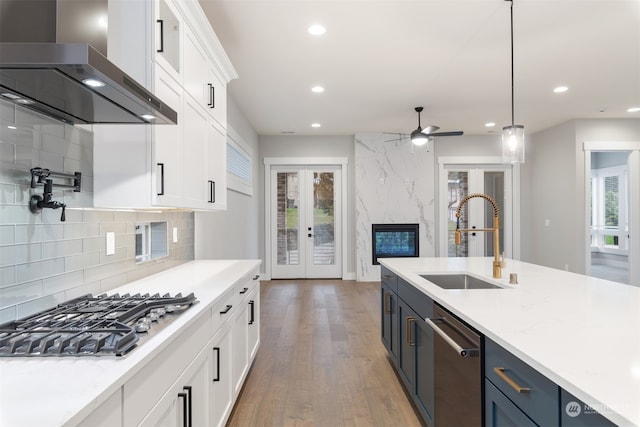 kitchen featuring pendant lighting, wall chimney range hood, sink, appliances with stainless steel finishes, and white cabinets