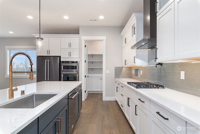 kitchen with sink, white cabinetry, decorative light fixtures, appliances with stainless steel finishes, and wall chimney range hood