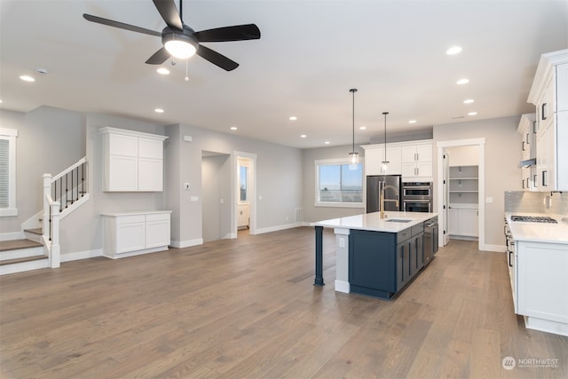 kitchen featuring white cabinetry, stainless steel appliances, hanging light fixtures, and a center island with sink