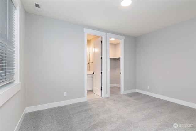 unfurnished bedroom featuring a spacious closet, light colored carpet, and a closet