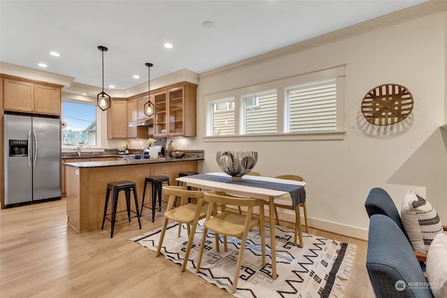 kitchen with a breakfast bar, crown molding, decorative light fixtures, stainless steel fridge, and light hardwood / wood-style floors