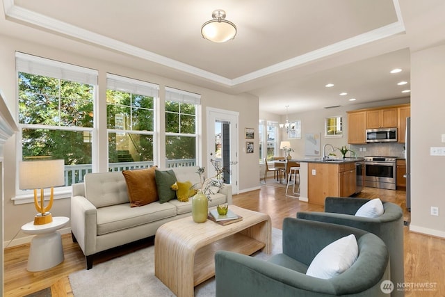 living area featuring baseboards, a tray ceiling, recessed lighting, a notable chandelier, and light wood-type flooring