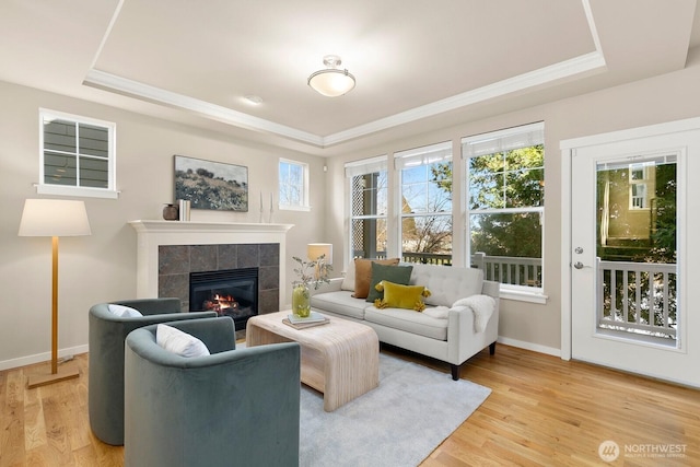 living room featuring baseboards, light wood-type flooring, a tray ceiling, ornamental molding, and a fireplace