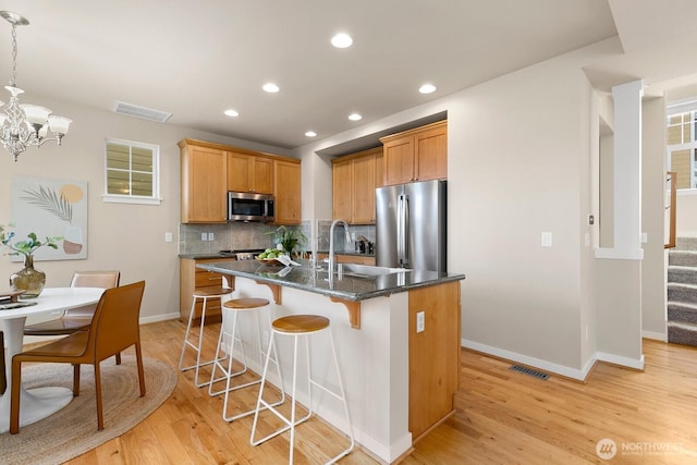 kitchen featuring tasteful backsplash, a breakfast bar area, light wood-style flooring, appliances with stainless steel finishes, and a sink