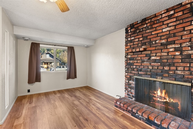 unfurnished living room featuring hardwood / wood-style flooring, ceiling fan, a brick fireplace, and a textured ceiling