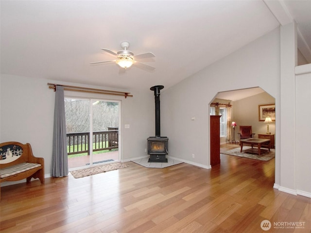 living area with arched walkways, lofted ceiling, a ceiling fan, a wood stove, and light wood-type flooring