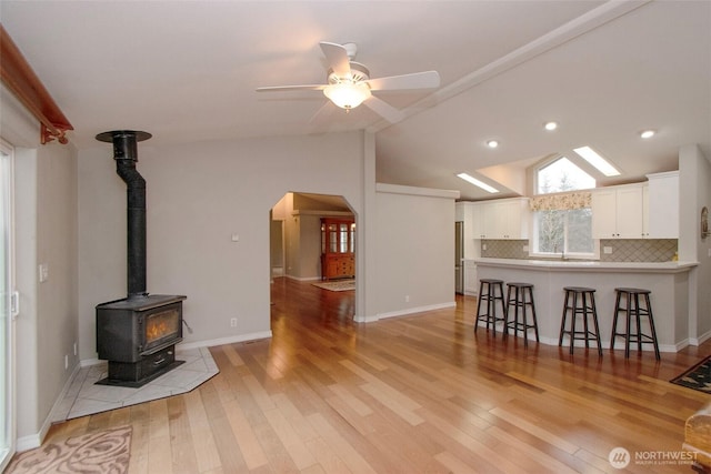 living area with ceiling fan, arched walkways, light wood-style flooring, vaulted ceiling, and a wood stove