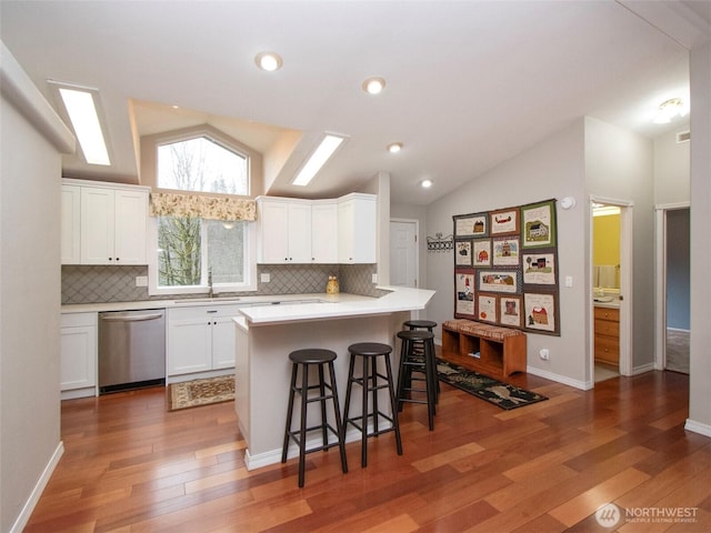 kitchen featuring a kitchen breakfast bar, light countertops, stainless steel dishwasher, and white cabinets