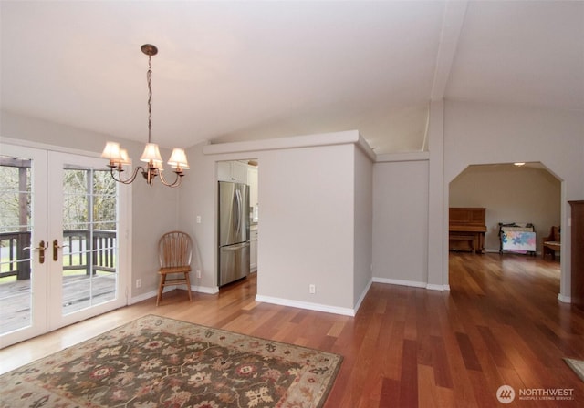 unfurnished dining area featuring arched walkways, vaulted ceiling, baseboards, and wood finished floors