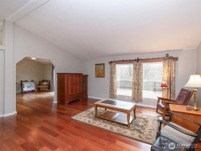 living room with arched walkways, vaulted ceiling, baseboards, and wood finished floors