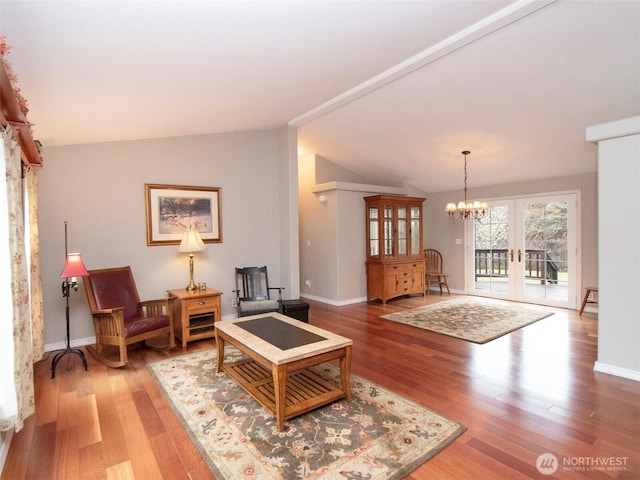 living area with an inviting chandelier, vaulted ceiling, wood finished floors, and french doors