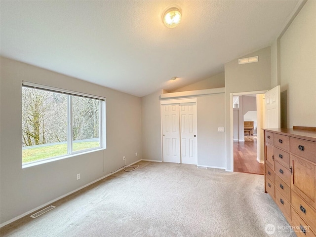 unfurnished bedroom featuring light carpet, baseboards, visible vents, vaulted ceiling, and a closet