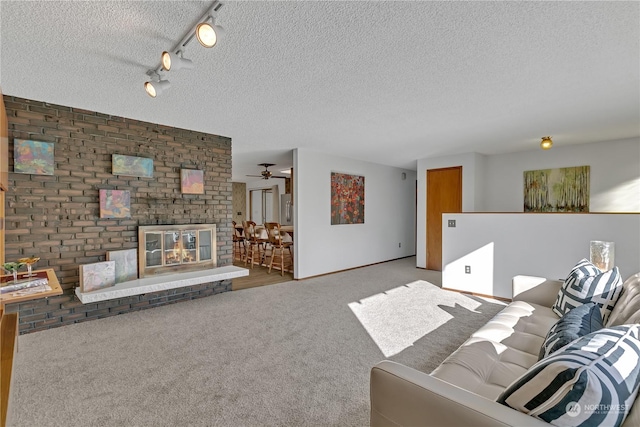 living room with rail lighting, carpet, a brick fireplace, and a textured ceiling