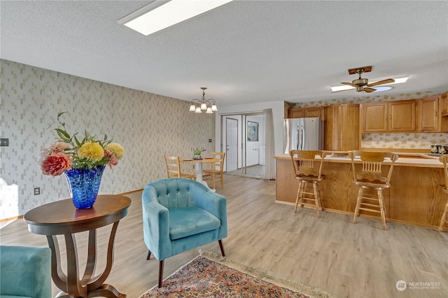 kitchen with a kitchen bar, a textured ceiling, hanging light fixtures, stainless steel refrigerator, and light hardwood / wood-style flooring