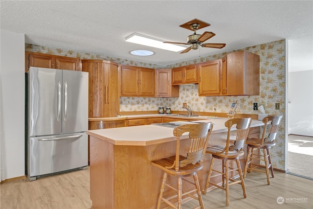 kitchen with a breakfast bar, stainless steel fridge, light hardwood / wood-style floors, and kitchen peninsula