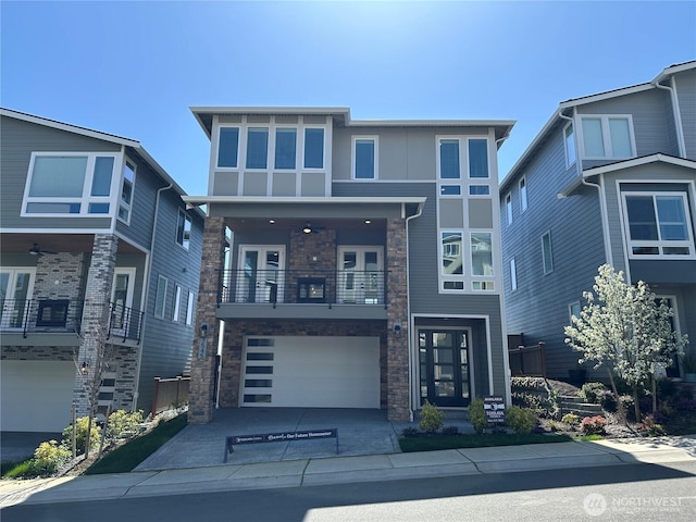 view of front facade with a balcony, driveway, stone siding, french doors, and a garage