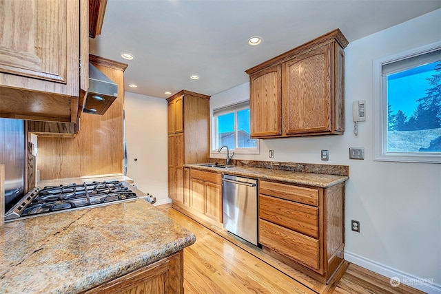 kitchen featuring sink, wall chimney range hood, stainless steel appliances, light stone counters, and light wood-type flooring