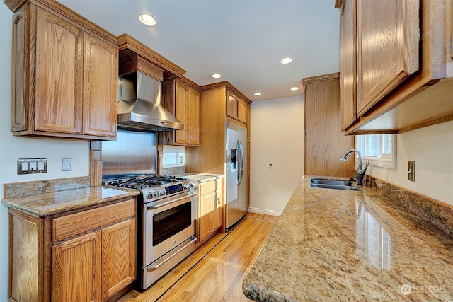 kitchen with ventilation hood, sink, light stone counters, stainless steel appliances, and light hardwood / wood-style flooring