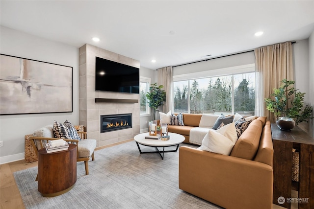 living room with a tile fireplace, a healthy amount of sunlight, and light wood-type flooring