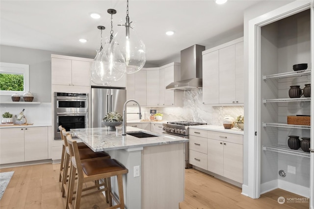 kitchen featuring sink, white cabinetry, high end appliances, a center island with sink, and wall chimney exhaust hood