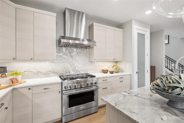 kitchen with high end stainless steel range, tasteful backsplash, light stone counters, light wood-type flooring, and wall chimney range hood