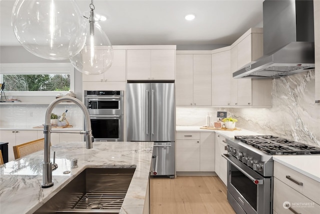 kitchen with sink, tasteful backsplash, appliances with stainless steel finishes, wall chimney range hood, and white cabinets