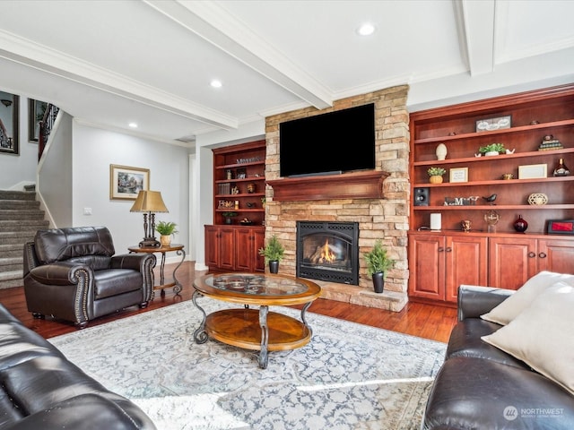 living area with a stone fireplace, wood finished floors, ornamental molding, stairway, and beam ceiling