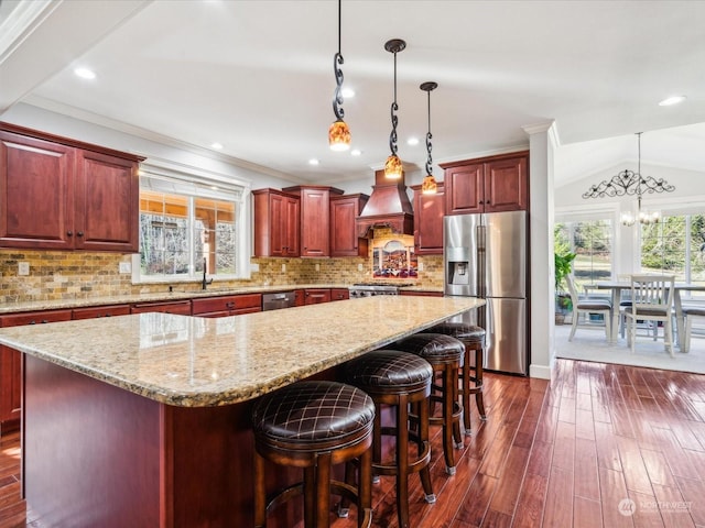 kitchen with reddish brown cabinets, a center island, dark wood-style floors, stainless steel fridge, and premium range hood