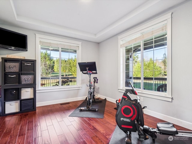 workout room featuring a raised ceiling, dark wood finished floors, visible vents, and baseboards