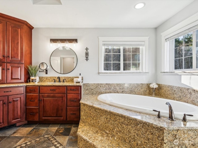 bathroom with stone tile flooring, recessed lighting, a bath, and vanity