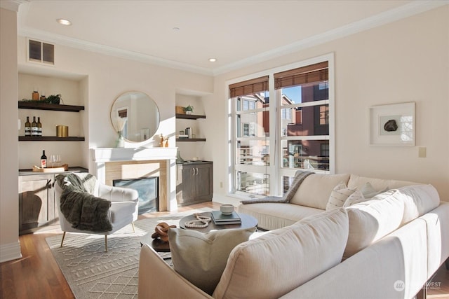 living room with a premium fireplace, hardwood / wood-style floors, crown molding, and built in shelves