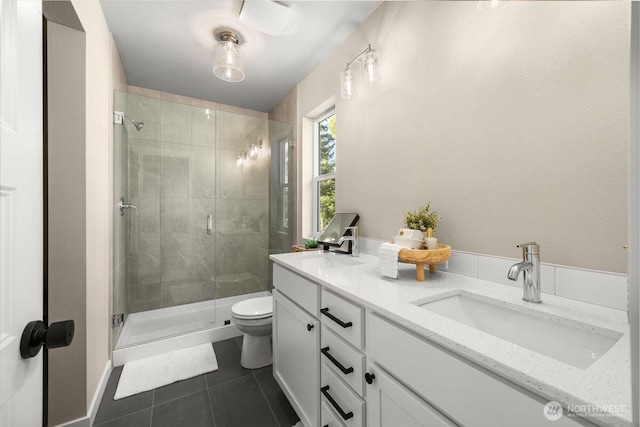 bathroom featuring tile patterned flooring, double vanity, toilet, a shower stall, and a sink