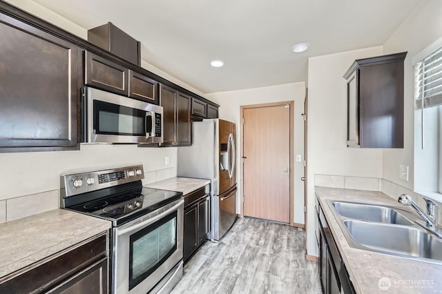 kitchen with light wood finished floors, stainless steel appliances, dark brown cabinets, light countertops, and a sink