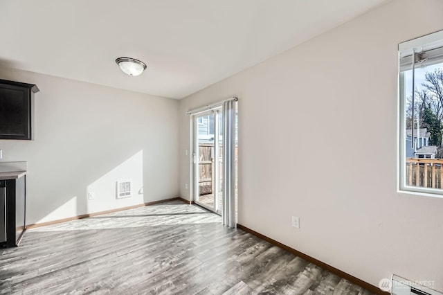 interior space with a baseboard radiator, baseboards, visible vents, and wood finished floors