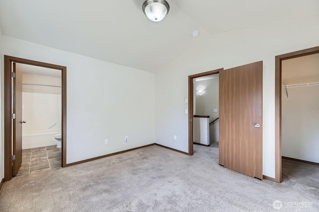 unfurnished bedroom featuring a closet, light colored carpet, a spacious closet, ensuite bathroom, and vaulted ceiling