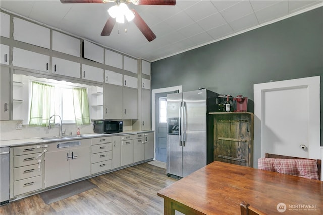 kitchen featuring wood finished floors, a sink, light countertops, appliances with stainless steel finishes, and open shelves