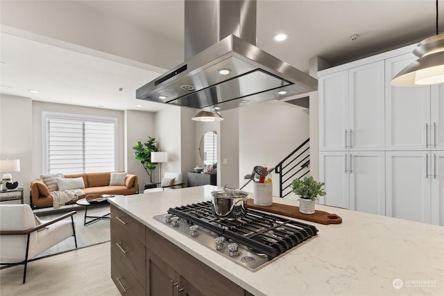 kitchen with pendant lighting, island range hood, stainless steel gas stovetop, white cabinets, and light stone counters