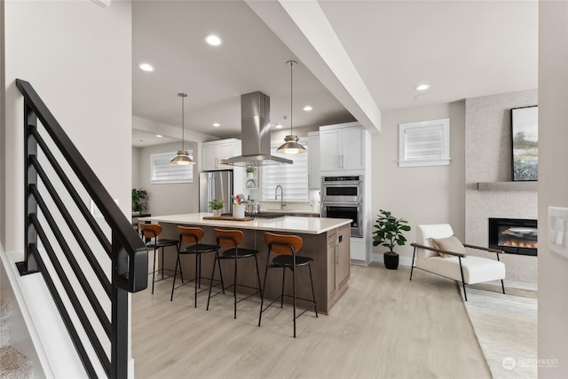 kitchen with appliances with stainless steel finishes, white cabinetry, island range hood, a kitchen island, and decorative light fixtures