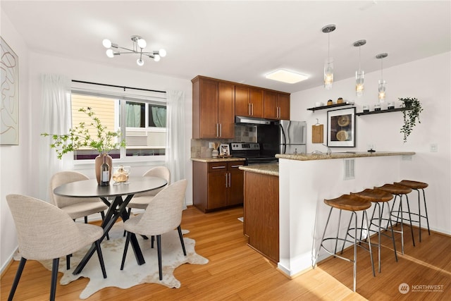 kitchen with appliances with stainless steel finishes, decorative backsplash, hanging light fixtures, light stone counters, and light hardwood / wood-style floors