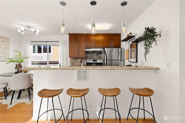 kitchen featuring pendant lighting, tasteful backsplash, kitchen peninsula, stainless steel appliances, and light hardwood / wood-style flooring