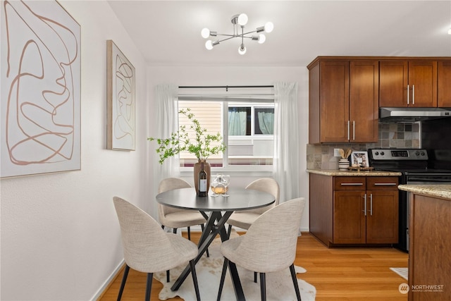 kitchen with stainless steel electric range oven, a chandelier, light stone countertops, light hardwood / wood-style floors, and backsplash